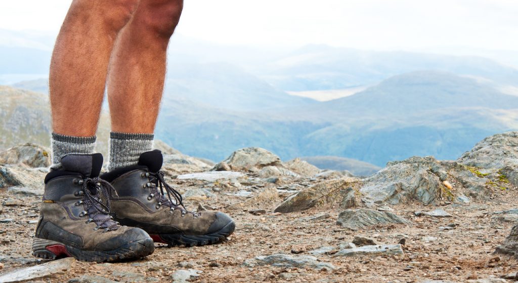 A photo of a man's calfs and hiking boots while standing above an epic fjord.