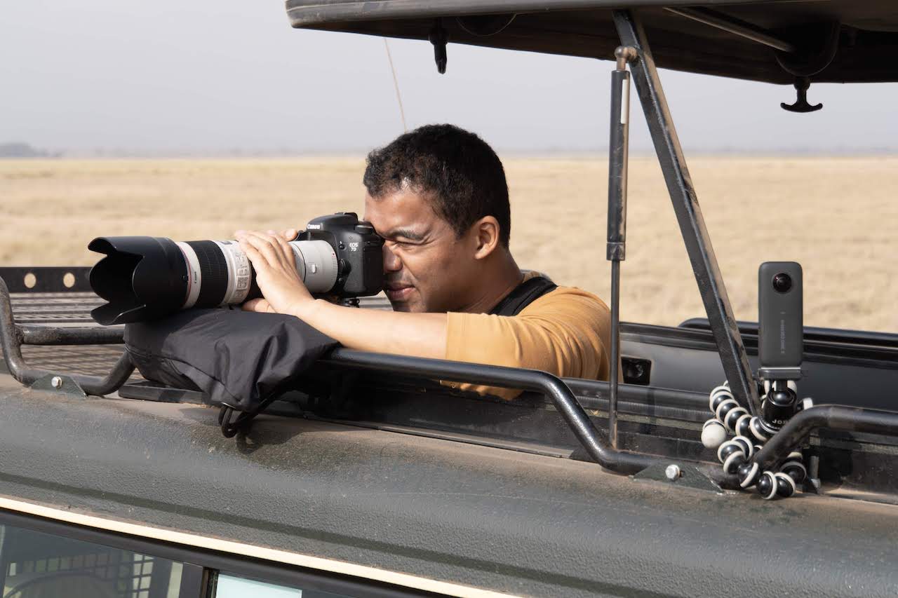 A photographer steadies his lens as he attempts to shoot a distant, unseen animal in the Masai Mara.